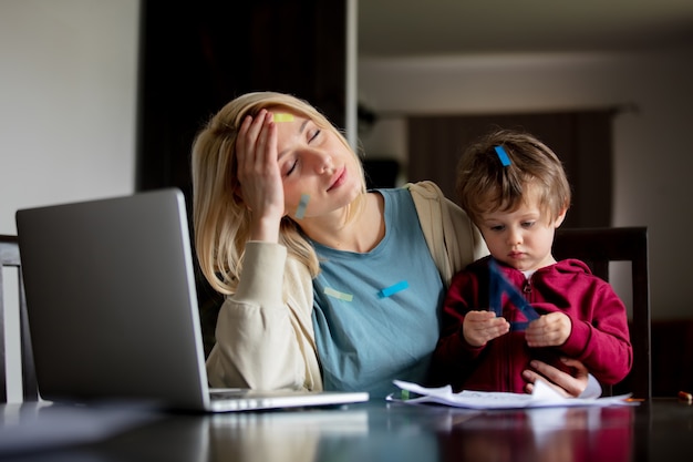 Junge Mutter arbeitet mit ihrem Kind zu Hause am Computer