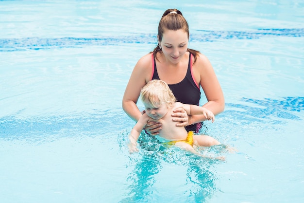 Junge Mutter bringt ihrem kleinen Sohn bei, wie man in einem Schwimmbad schwimmt