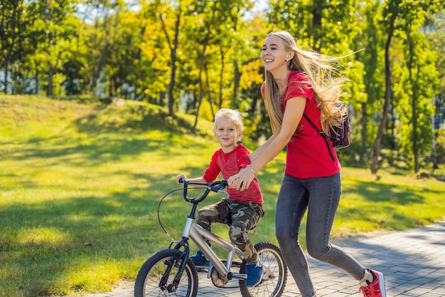Junge Mutter bringt ihrem Sohn bei, wie man im Park Fahrrad fährt.