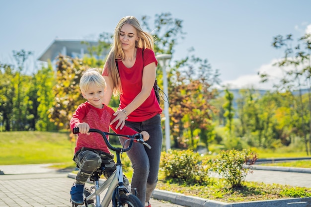 Junge Mutter bringt ihrem Sohn bei, wie man im Park Fahrrad fährt