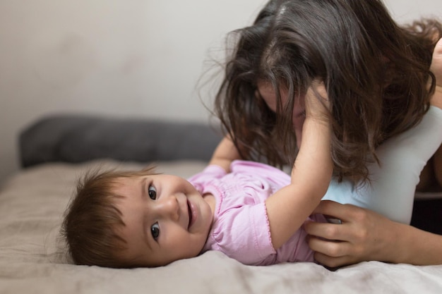 Junge Mutter der glücklichen liebevollen Familie, die mit ihrem Baby im Schlafzimmer spielt