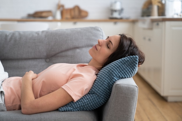 Junge Mutter, die auf einer Couch liegt, sich ausruht, zu Hause schläft.