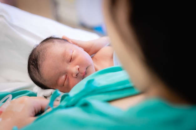 Junge Mutter, die ihr neugeborenes Baby hält, das die ersten Tage des Lebens im Krankenhaus schläft