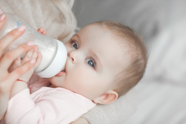 Junge Mutter, die ihre kleine nette Babytochter mit Flasche Kinderformel einzieht. Frau mit ihrem neugeborenen Baby zu Hause. Mutter, die auf ein Kind aufpasst. Alternative zum Stillen.