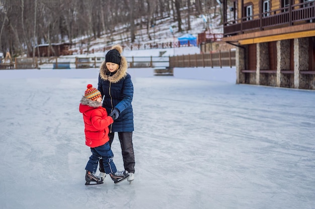 Junge Mutter, die ihrem kleinen Sohn Eislaufen auf der Eisbahn im Freien beibringt Familie genießt den Winter auf der Eisbahn im Freien