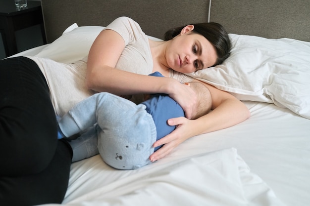 Junge Mutter, die ihren Sohn stillt, Mutter stillende Umarmung Baby, Mutter und Kleinkind liegen zusammen zu Hause auf dem Bett, Baby essen und einschlafen