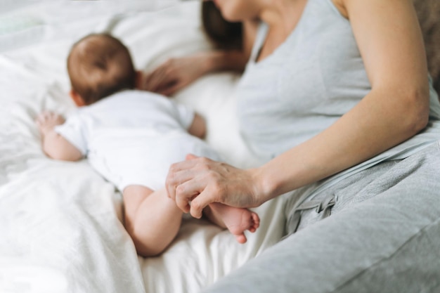 Foto junge mutter, die sich mit süßem baby im bett amüsiert. natürliche töne, liebe, emotionen, selektiver fokus.