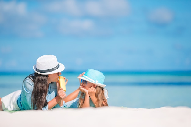 Junge Mutter, die Sonnencreme an der Tochternase auf dem Strand aufträgt. Sonnenschutz