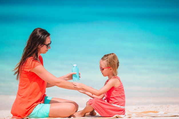 Junge Mutter, die Sonnencreme auf Tochternase am Strand anwendet. Sonnenschutz