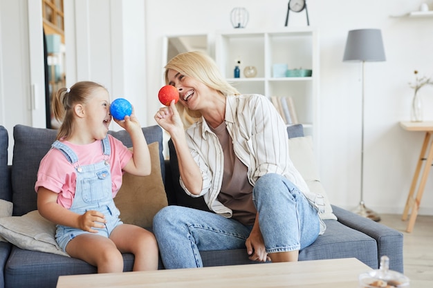 Junge Mutter, die Spaß zusammen mit ihrer Tochter mit Down-Syndrom hat, während sie auf Sofa im Zimmer sitzen