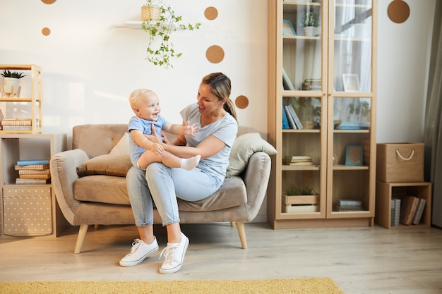 Junge Mutter, die Zeit zu Hause verbringt, sitzt auf Sofa mit ihrem kleinen Sohn im Wohnzimmer