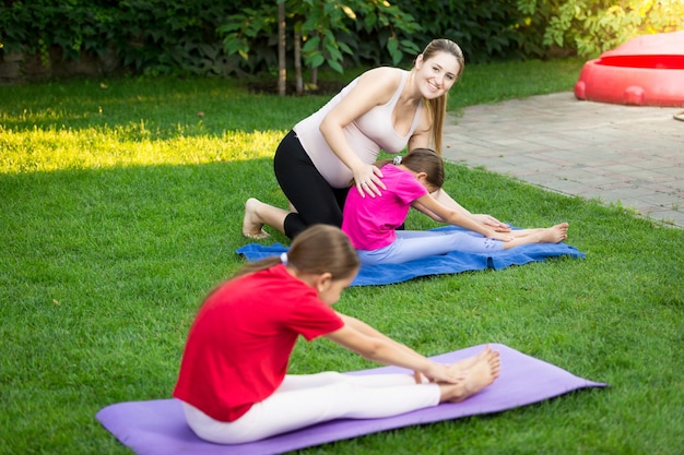 Junge Mutter, die zwei Töchter im Park Yoga unterrichtet