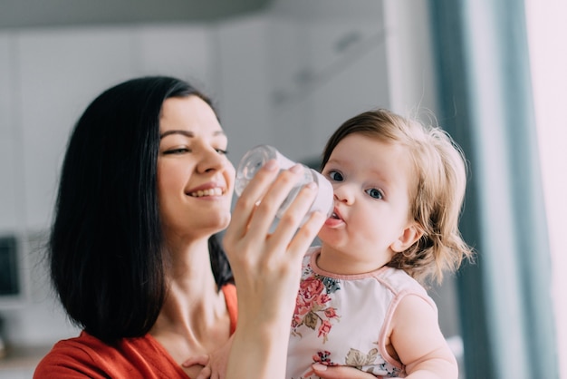 Junge Mutter füttert ihr Baby aus der Flasche in der Küche