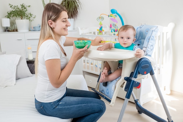 Junge Mutter füttert ihr Baby mit Fruchtsauce im Hochstuhl