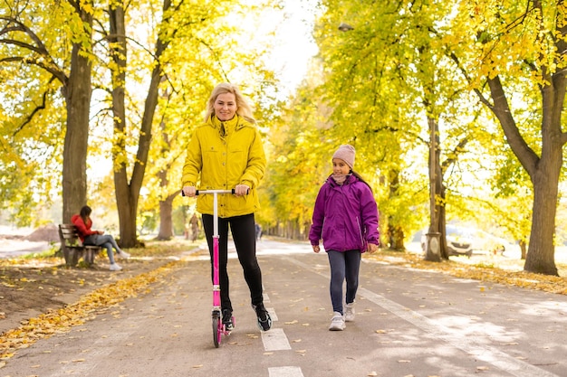 Junge Mutter geht mit ihrer Tochter auf einem Kleinkinderroller im Park spazieren.