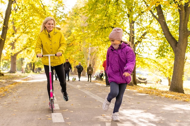Junge mutter geht mit ihrer tochter auf einem kleinkinderroller im park spazieren.