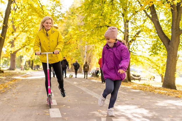 Junge Mutter geht mit ihrer Tochter auf einem Kleinkinderroller im Park spazieren.