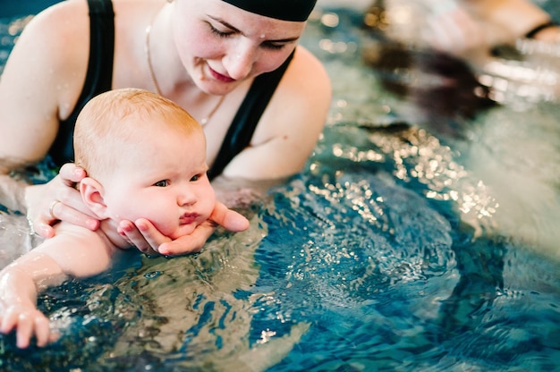 Junge Mutter, glückliches kleines Mädchen im Pool. Bringt dem Kleinkind das Schwimmen bei.