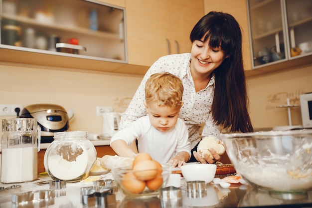 junge Mutter in einem weißen Hemd, das zu Hause Lebensmittel in der Küche mit ihrem kleinen Sohn vorbereitet