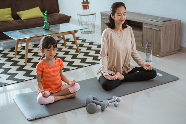 Junge Mutter macht Yoga-Übung zu Hause mit ihrer Tochter zusammen