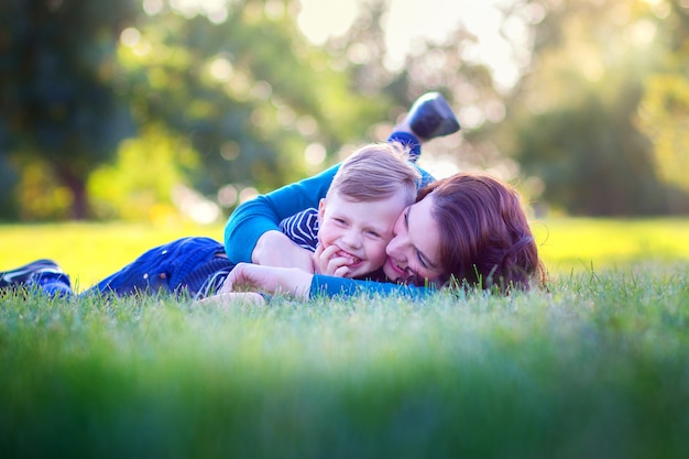 Junge Mutter mit dem Sohn liegen auf einem Gras im Park und umfassen freudig