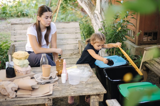 Junge Mutter mit ihrer kleinen Tochter, die sich darauf vorbereitet, verschiedene Arten von Müll zu recyceln und zu setzen?
