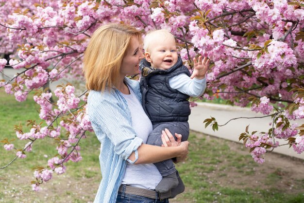 Junge Mutter mit kleinem Sohn im Park mit Sakura-Kirschblütenbaum Glückliche Mutter und Kind