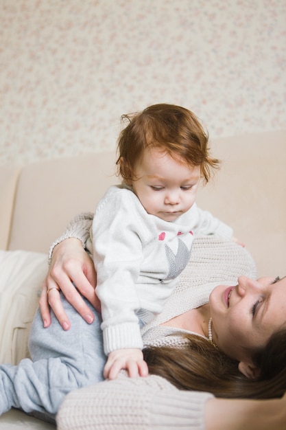 Junge Mutter mit kleinen Kindern auf Händen, die auf Sofa sitzen. Junge Frau mit Tochter