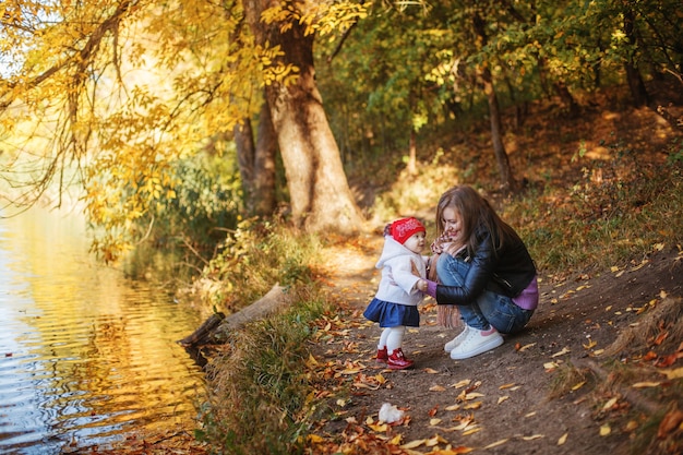 Junge Mutter mit kleiner Tochter auf einem Spaziergang im Park am Teich im Herbst