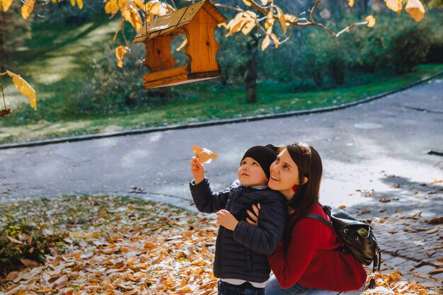 Junge Mutter mit Kleinkind legte Samen in Vogelhäuschen. Herbstsaison