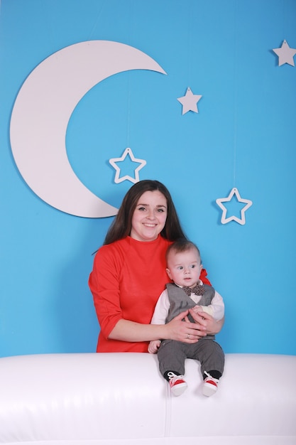 Junge Mutter mit niedlichem Baby auf einem weißen Sofa. blaue Wand mit einem weißen Mond und Sternen an einer Wand.