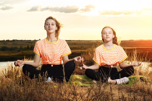 Junge Mutter mit Tochter, die Yoga im Freien macht