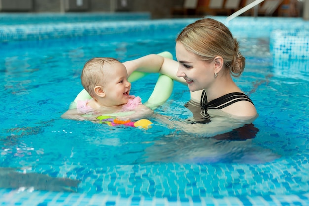 Junge Mutter, Schwimmlehrer und glückliches kleines Mädchen im Pool. Bringt Säuglingen das Schwimmen bei.