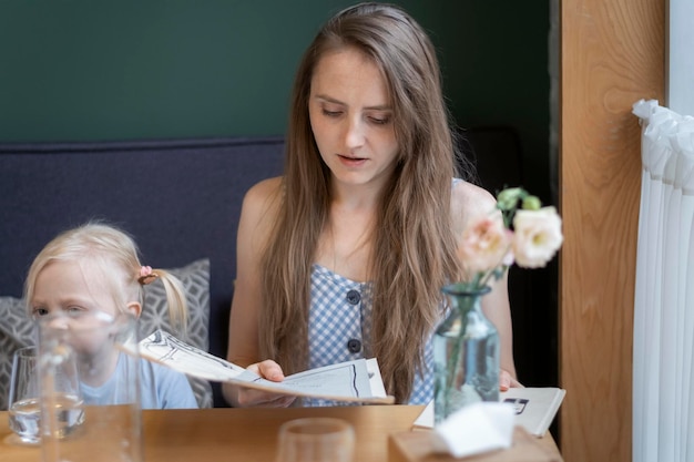 Junge Mutter sitzt mit Tochter am Tisch im Café und liest die Speisekarte Frau macht eine Bestellung im Restaurant