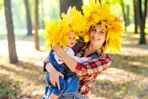 junge Mutter spielt mit Baby im Herbstpark mit Kranz der Blätter