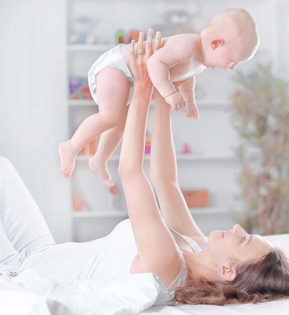 junge mutter spielt mit dem baby, das auf dem bett liegt. das Konzept der Bildung