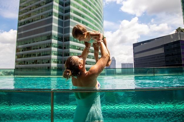 Junge Mutter spielt mit kleiner Tochter im Pool auf dem Dach in Megapolis City