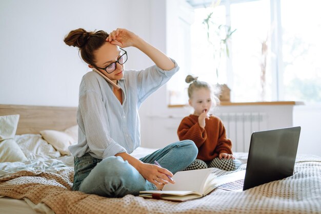 Junge Mutter telefoniert und bespricht Arbeitsprobleme, während sie sich um ihr Kind Covid19 kümmert