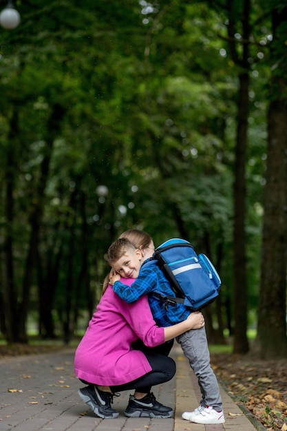 Junge Mutter umarmt ihren aufgeregten erstklassigen Sohn auf dem Weg zur Schule, bereit zum Lernen