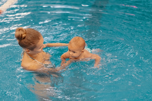 Junge Mutter und ihr Baby genießen eine Babyschwimmstunde im Pool. Kind, das Spaß im Wasser mit Mutter hat