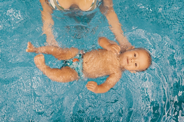 Junge Mutter und ihr Baby genießen eine Babyschwimmstunde im Pool. Kind, das Spaß im Wasser mit Mutter hat