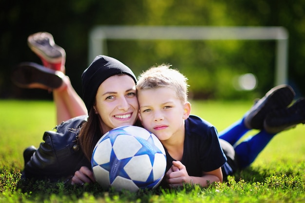 Junge Mutter und ihr kleiner Junge, die ein Fußballspiel am sonnigen Sommertag spielt. Familie, die Spaß mit Ball draußen hat