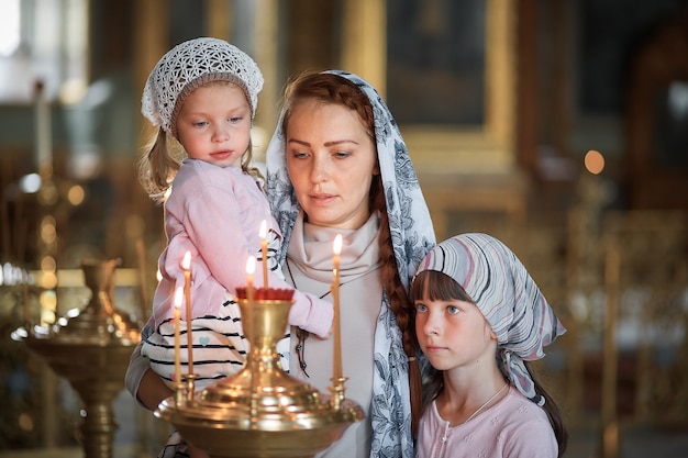 Junge Mutter und ihre kleine blonde kaukasische Tochter mit Kerzen in der orthodoxen russischen Kirche
