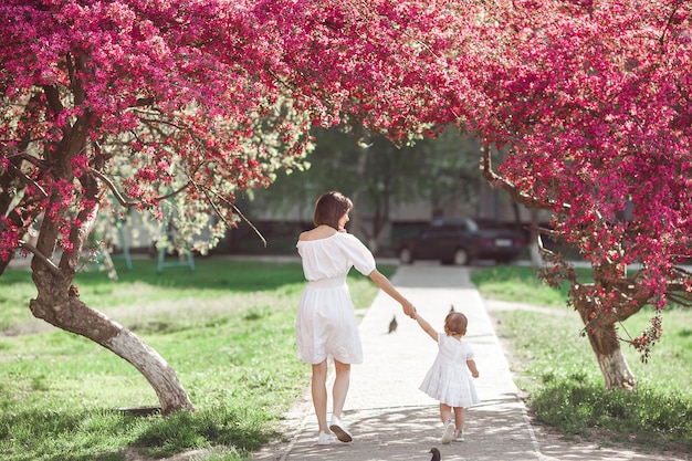 Junge Mutter und ihre kleine Tochter, die zusammen im Frühjahr in die Zeit des Parks geht. Glückliche Familie im Freien. Lieben mit entzückendem Baby.