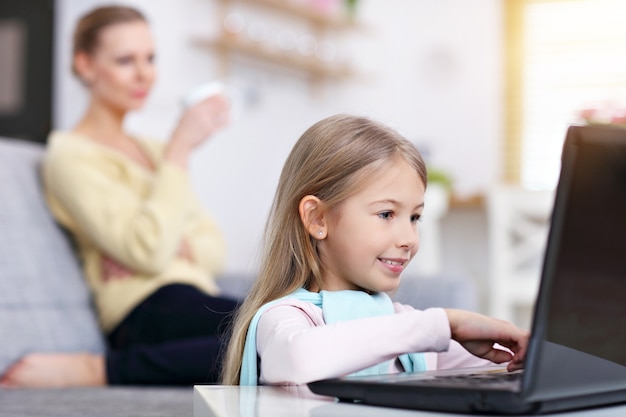 Junge mutter und ihre kleine tochter mit laptop und sitzen auf dem sofa zu hause