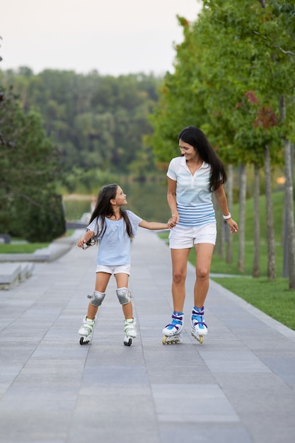 Junge Mutter und ihre kleine Tochter Rollerskaten im Park