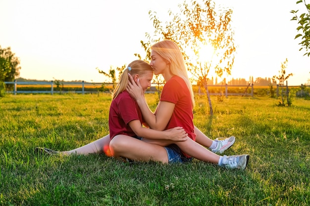 Junge Mutter und ihre Tochter sitzen bei Sonnenuntergang auf den Knien auf dem Feld