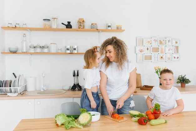 Junge Mutter und ihre zwei Kinder, die Gemüsesalat machen