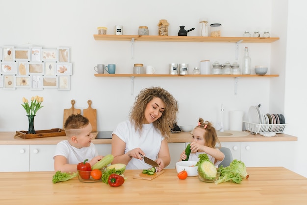 Junge Mutter und ihre zwei Kinder, die Gemüsesalat machen