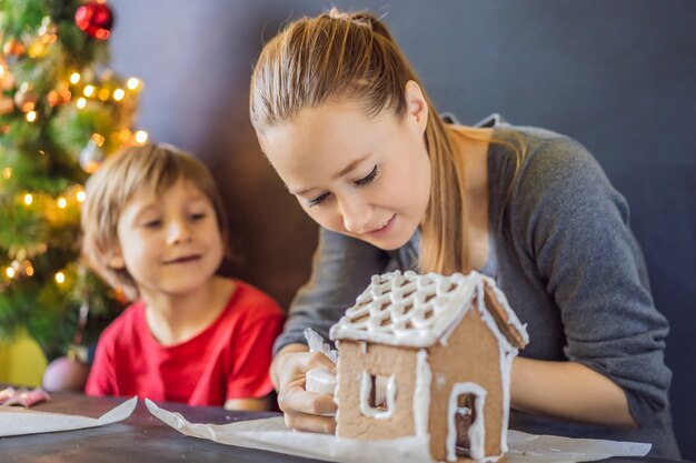 Junge Mutter und Kind machen Lebkuchenhaus am Heiligabend